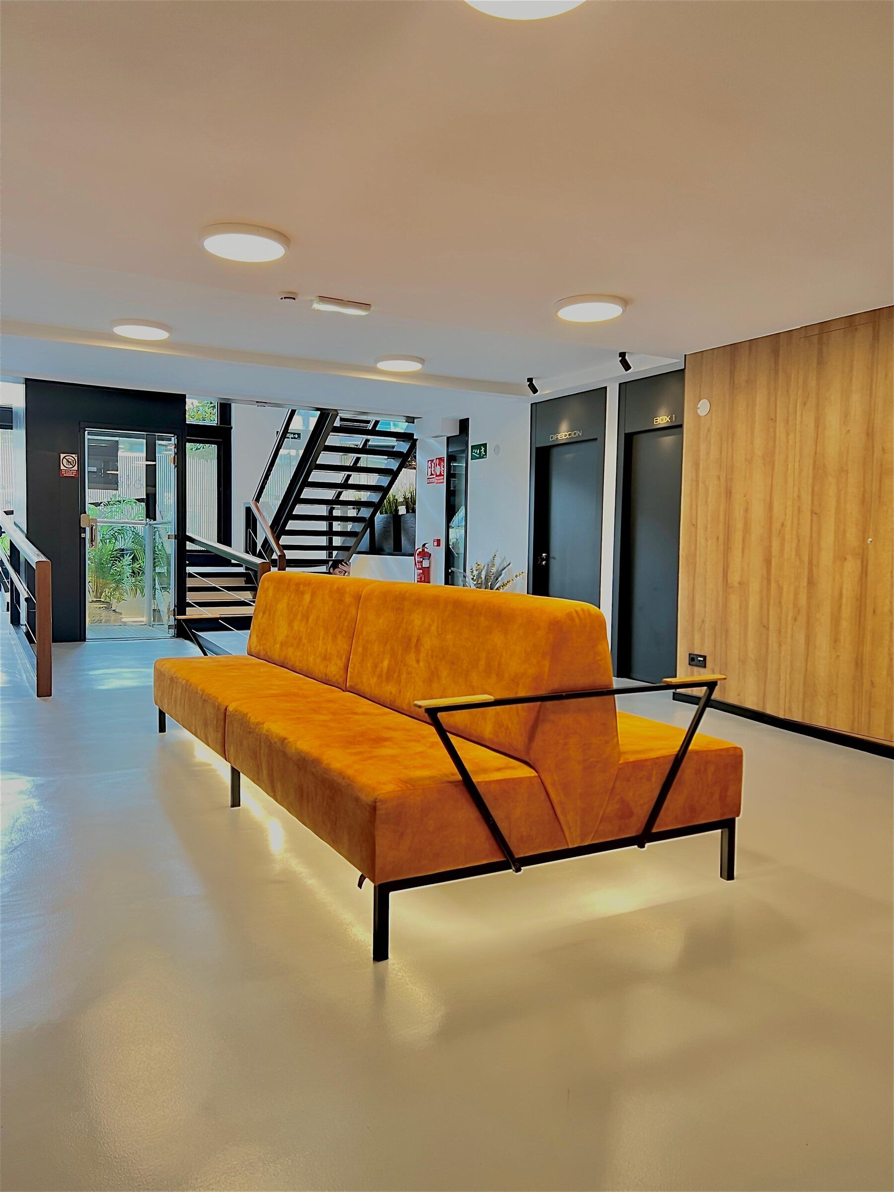 Sala de espera de la primera planta con sofá naranja y escalera al fondo