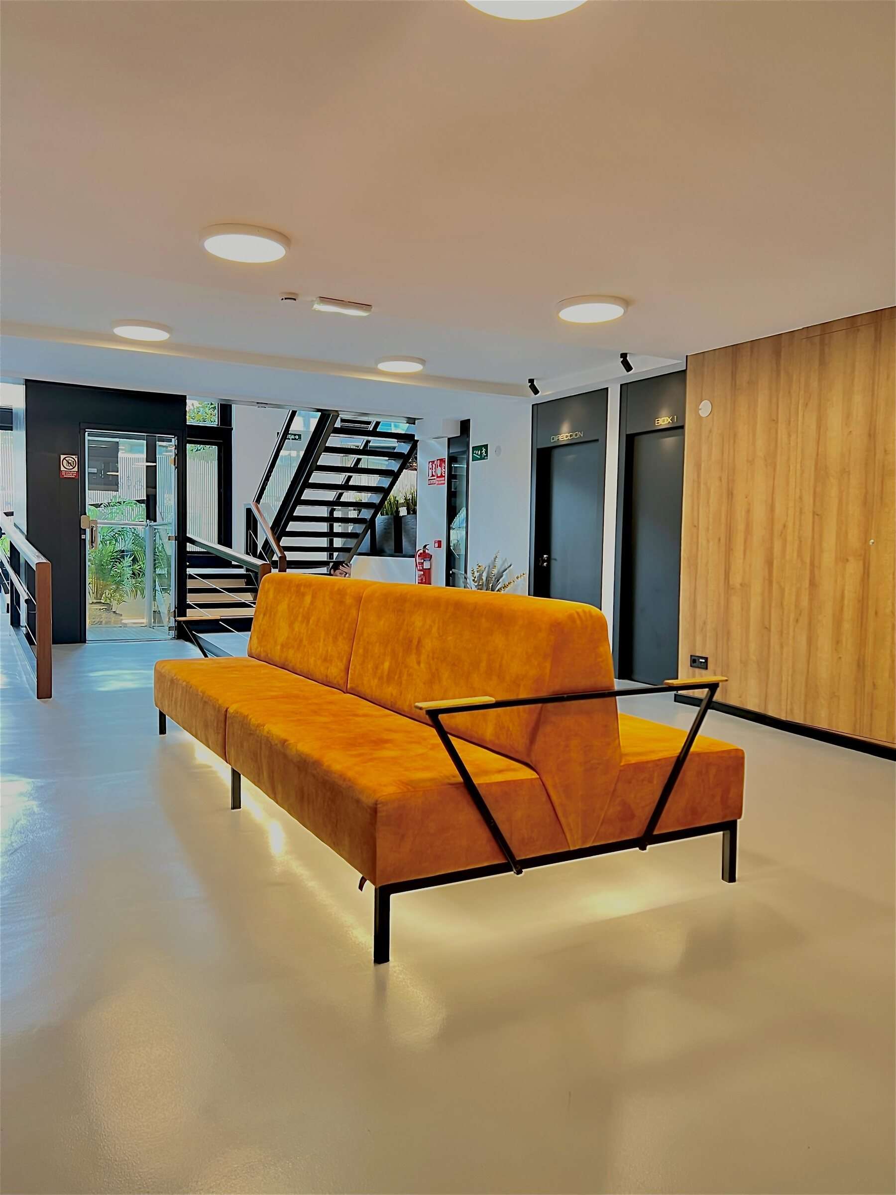 Sala de espera de la primera planta con sofá naranja y escalera